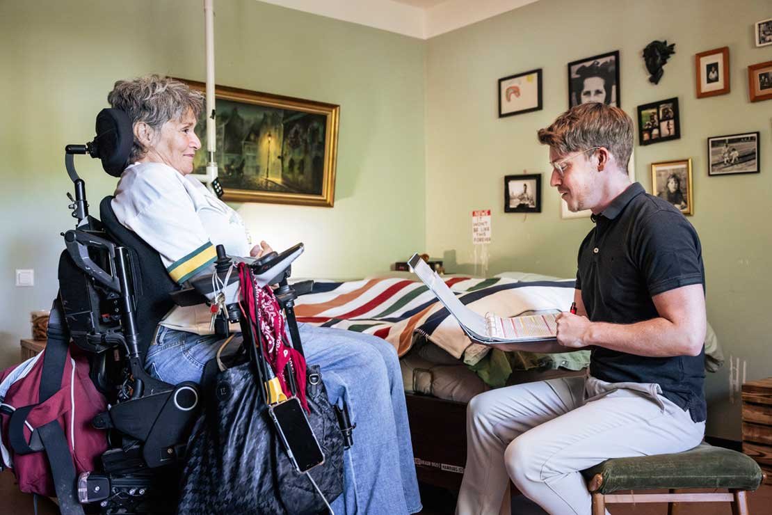 Eine Frau im Rollstuhl im Gespräch mit einem gegenüber sitzenden Mann
